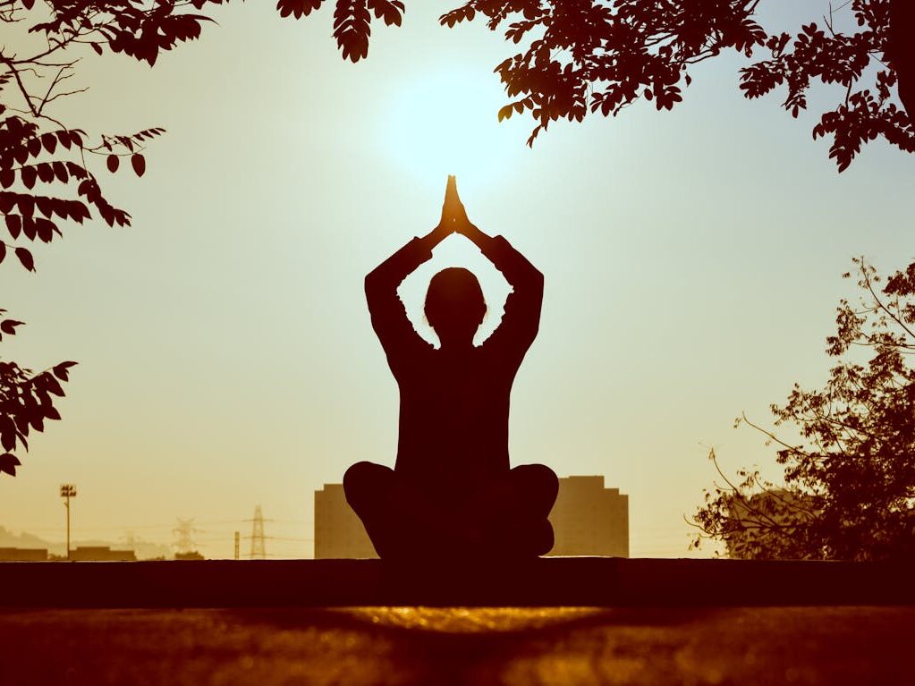 Silhouette of a person practicing yoga outdoors during sunrise, creating a calming atmosphere.